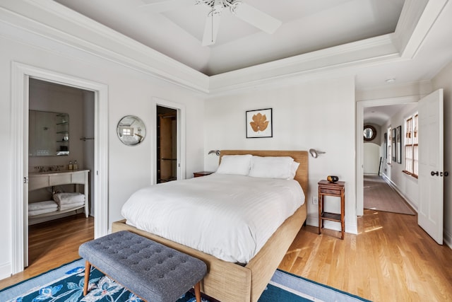 bedroom featuring ensuite bathroom, ornamental molding, a raised ceiling, ceiling fan, and light hardwood / wood-style floors