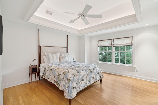 bedroom with wood-type flooring, ornamental molding, ceiling fan, and a tray ceiling