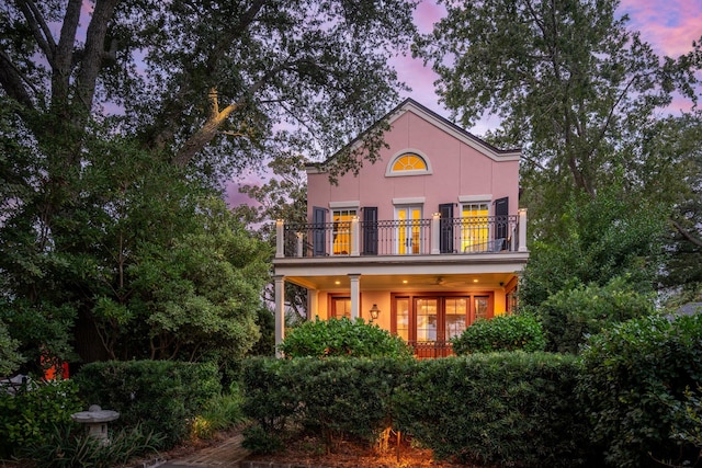 back house at dusk featuring french doors, a balcony, and ceiling fan