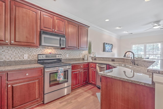 kitchen with kitchen peninsula, appliances with stainless steel finishes, light stone countertops, crown molding, and sink