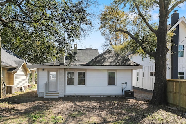 back of property with a shingled roof, fence, entry steps, central AC unit, and a chimney