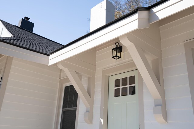 view of exterior entry with a chimney and a shingled roof