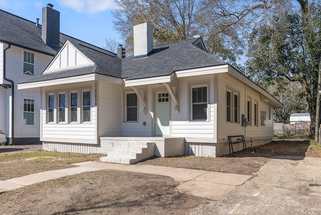 view of front of house featuring covered porch, roof with shingles, a chimney, and fence