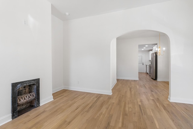 unfurnished living room featuring a fireplace, light wood-style flooring, baseboards, and arched walkways