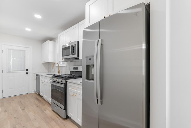 kitchen with light countertops, light wood-style flooring, stainless steel appliances, white cabinetry, and a sink