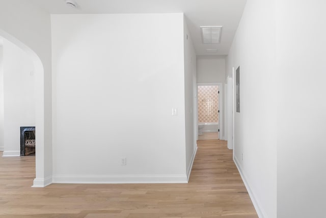 hallway featuring visible vents, baseboards, arched walkways, and light wood finished floors