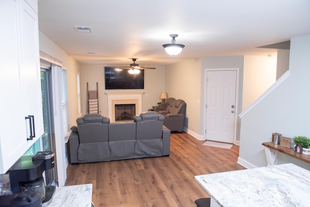living room featuring light wood-style floors, ceiling fan, a fireplace, and baseboards