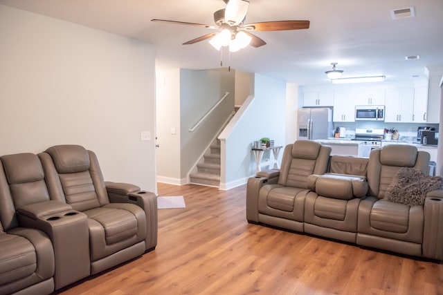 living room featuring a ceiling fan, stairs, light wood-type flooring, and baseboards