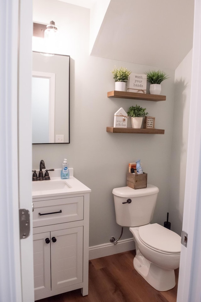 half bathroom with toilet, wood finished floors, baseboards, and vanity