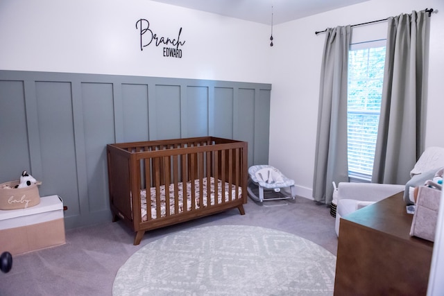 carpeted bedroom featuring a decorative wall, a nursery area, and a wainscoted wall
