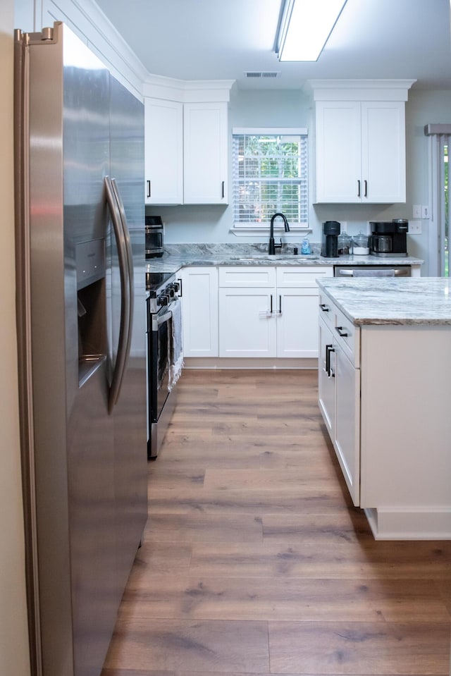 kitchen with appliances with stainless steel finishes, light wood-type flooring, light stone countertops, and white cabinetry