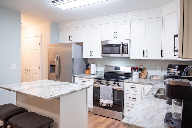 kitchen with appliances with stainless steel finishes, a center island, a kitchen breakfast bar, light wood-style flooring, and white cabinetry
