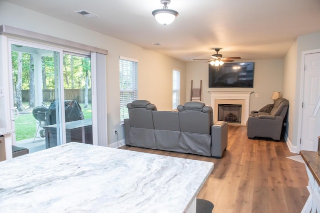 living area with ceiling fan, a fireplace, light wood-style floors, and baseboards