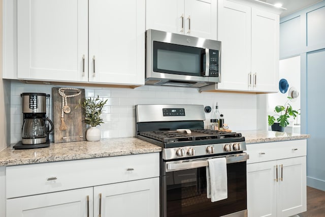 kitchen with light stone counters, stainless steel appliances, white cabinets, and decorative backsplash