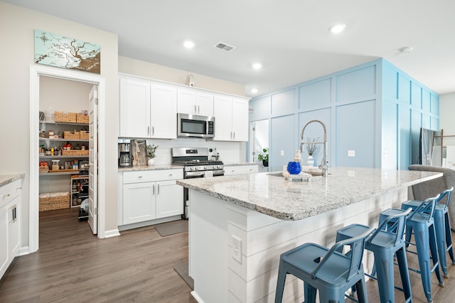 kitchen featuring visible vents, light stone countertops, a kitchen breakfast bar, stainless steel appliances, and a sink