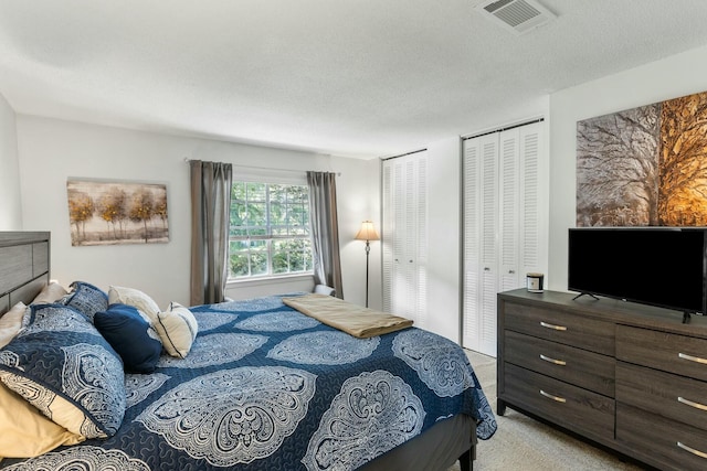 bedroom featuring visible vents, light colored carpet, a textured ceiling, and multiple closets