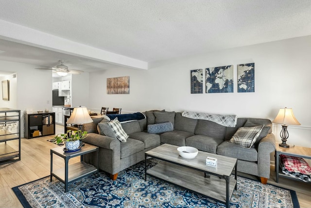 living room with light wood-type flooring, a textured ceiling, beamed ceiling, and a ceiling fan