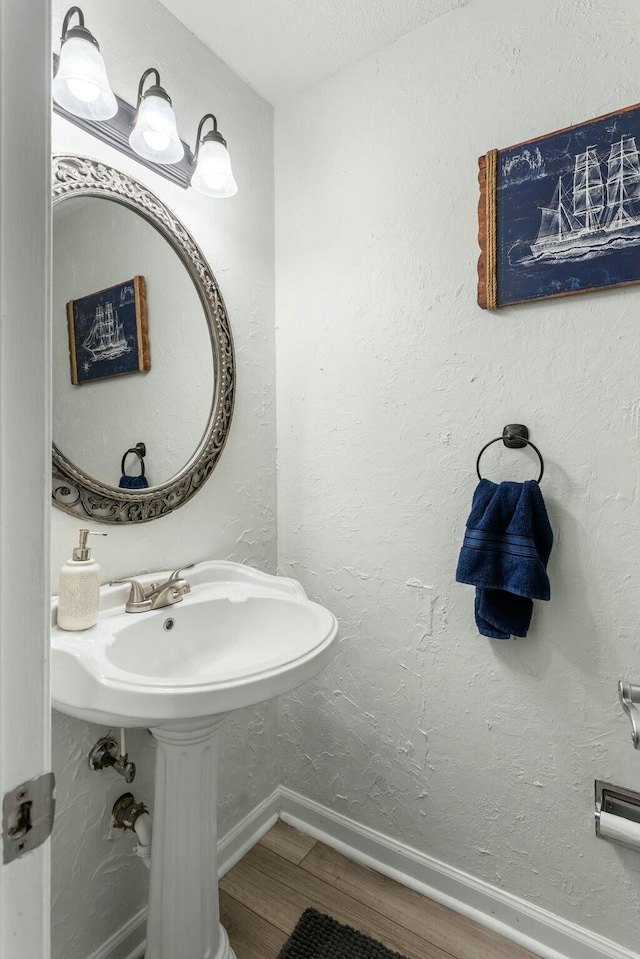 bathroom featuring a textured wall, baseboards, and wood finished floors