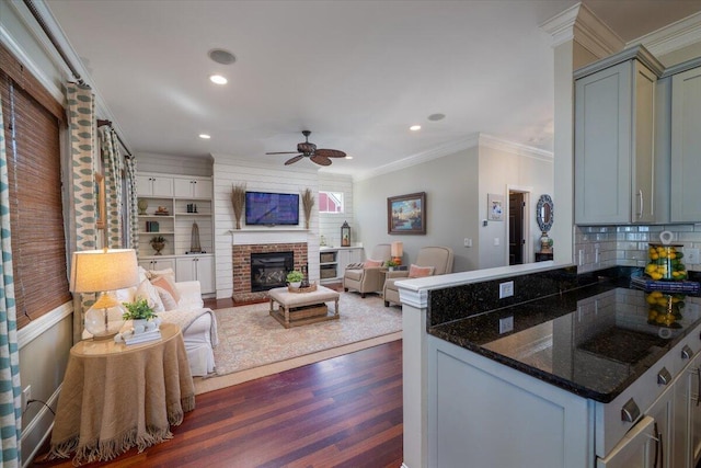 kitchen featuring gray cabinets, dark wood-type flooring, ornamental molding, a brick fireplace, and a peninsula