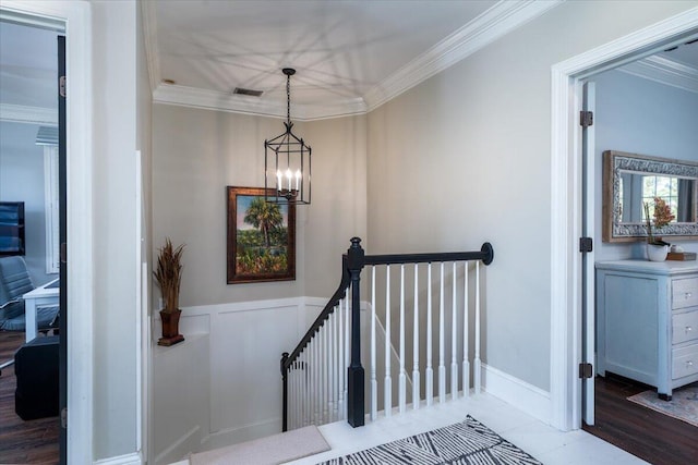 stairs featuring wood finished floors, visible vents, ornamental molding, wainscoting, and an inviting chandelier