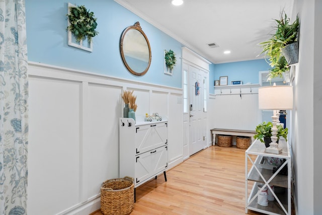 foyer entrance with a wainscoted wall, light wood-style flooring, a decorative wall, ornamental molding, and recessed lighting