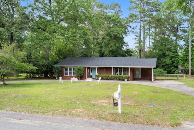 single story home featuring driveway, brick siding, and view of wooded area