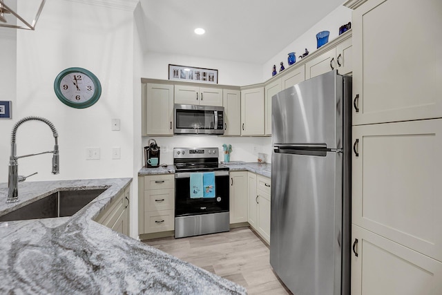 kitchen with light stone counters, stainless steel appliances, light wood-type flooring, and a sink