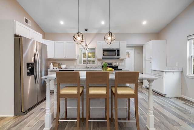 kitchen featuring white cabinetry, sink, stainless steel appliances, decorative light fixtures, and a kitchen island