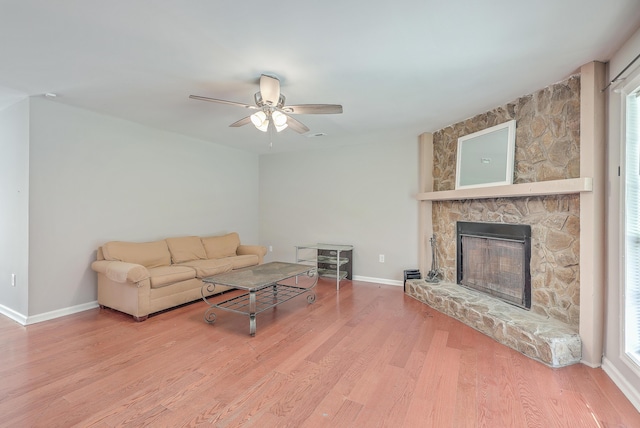 living area featuring ceiling fan, baseboards, a stone fireplace, and wood finished floors