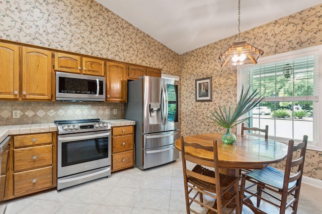 kitchen with lofted ceiling, appliances with stainless steel finishes, light tile patterned flooring, decorative light fixtures, and tile countertops