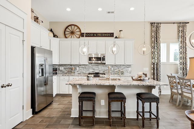 kitchen featuring white cabinets, tasteful backsplash, decorative light fixtures, and appliances with stainless steel finishes