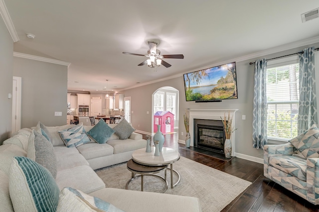 living area featuring baseboards, ornamental molding, dark wood finished floors, arched walkways, and plenty of natural light