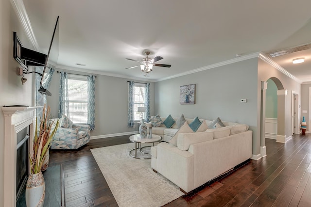 living room featuring arched walkways, crown molding, dark wood-type flooring, a ceiling fan, and a fireplace with flush hearth
