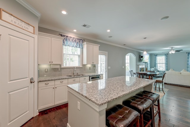 kitchen with a sink, a center island, ornamental molding, open floor plan, and arched walkways