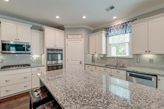 kitchen with stainless steel appliances, a sink, crown molding, white cabinets, and backsplash