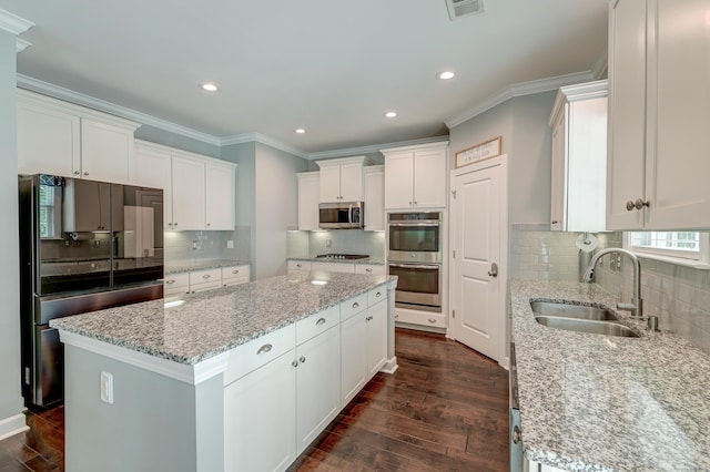 kitchen featuring appliances with stainless steel finishes, a sink, a kitchen island, tasteful backsplash, and crown molding