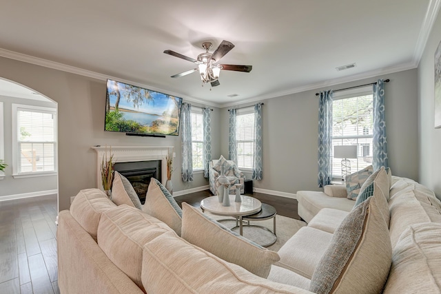 living room featuring arched walkways, baseboards, healthy amount of natural light, a ceiling fan, and ornamental molding