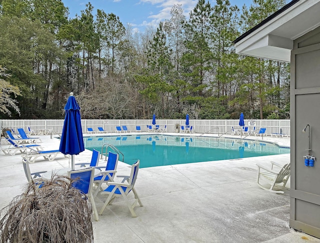community pool featuring a patio, fence, and view of wooded area