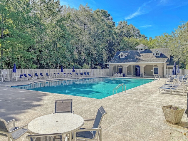 community pool featuring fence, a patio area, and view of scattered trees