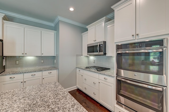kitchen with appliances with stainless steel finishes, ornamental molding, white cabinets, dark wood finished floors, and decorative backsplash