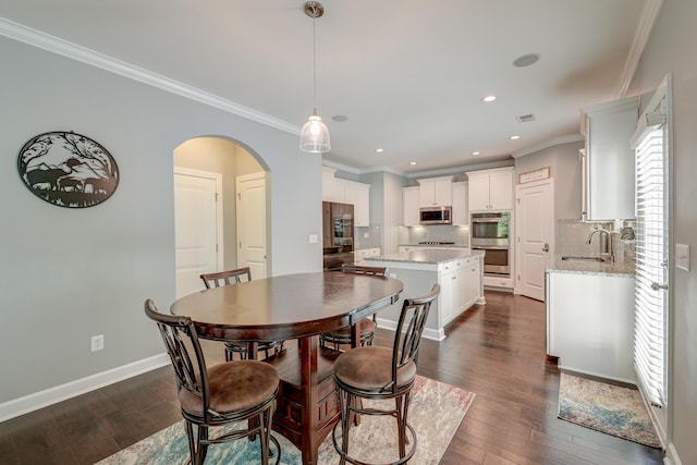 dining room featuring arched walkways, dark wood-style flooring, crown molding, recessed lighting, and baseboards