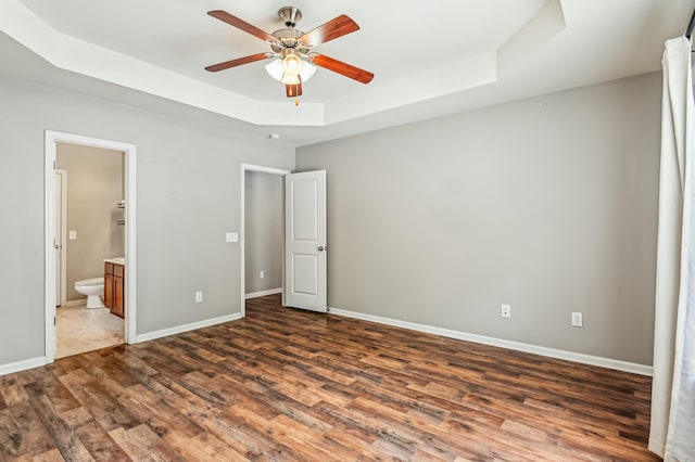 unfurnished bedroom with a raised ceiling, dark hardwood / wood-style flooring, ceiling fan, and ensuite bath