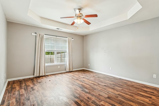 unfurnished room with dark wood-type flooring, ceiling fan, and a tray ceiling