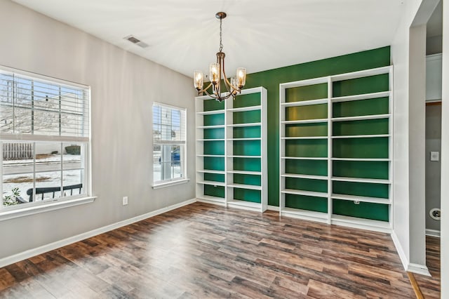 unfurnished room with a notable chandelier, a wealth of natural light, and dark hardwood / wood-style floors