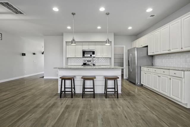 kitchen featuring decorative light fixtures, white cabinets, stainless steel appliances, and a kitchen island with sink