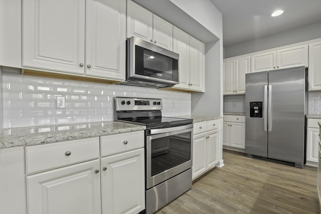 kitchen featuring white cabinetry, appliances with stainless steel finishes, decorative backsplash, light wood-type flooring, and light stone counters