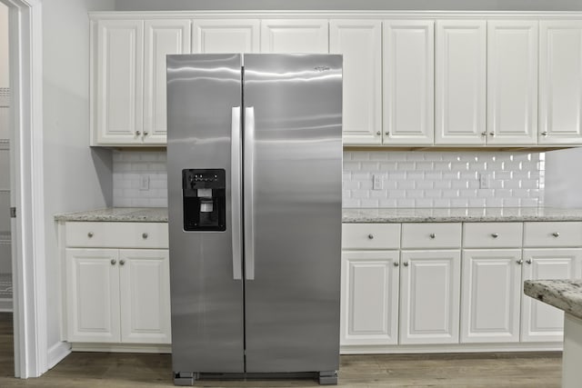 kitchen with decorative backsplash, stainless steel fridge, light stone counters, and white cabinetry