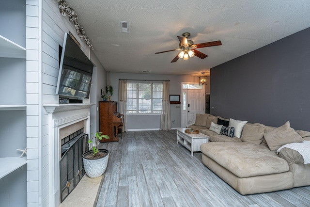 living area featuring visible vents, a fireplace with raised hearth, wood finished floors, a textured ceiling, and a ceiling fan