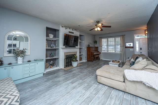 living area with a textured ceiling, a large fireplace, ceiling fan, and wood finished floors