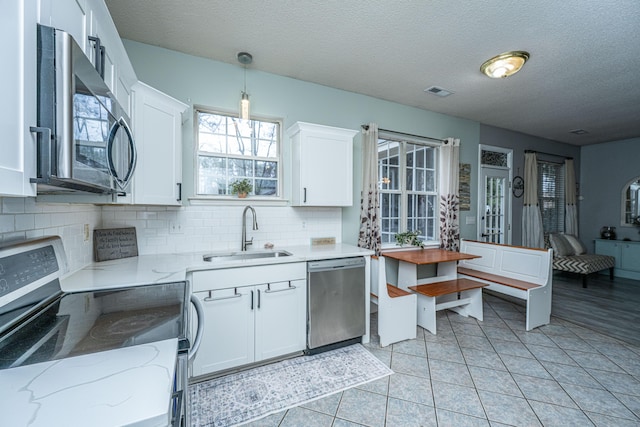 kitchen with a sink, backsplash, white cabinetry, appliances with stainless steel finishes, and light stone countertops